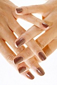 Close-up of woman's fingers interlaced wearing brown nail paint