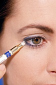 Close-up of hazel eyed woman spreading eyeliner with small sponge