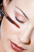 Close-up of woman wearing red lipstick applying mascara on eyelashes, eyes closed