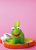 Kermit der Frosch liegt auf einem Blatt mit einer Tasse im Hintergrund