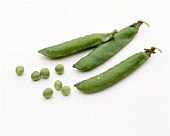 Three pea pods and loose peas on white background