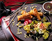 Spring rolls of scampi with vegetable on black plate served with soya sauce in bowl