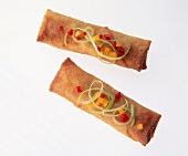 Deep fried spring rolls with diced peppers on white background