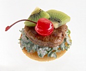 Close-up of toast with pork medallions, kiwi and cocktail cherry on white background