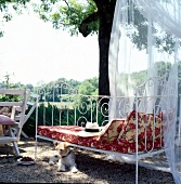 White painted iron bed on terrace with mosquito net and dog sitting under