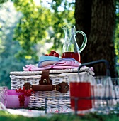 Picnic basket with berries and glass jug with juice in garden