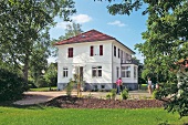Ein weißes zweistöckiges Haus im Grünen, Dach u. Fensterläden rot
