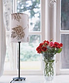 Tischlampe mit Blattmuster steht auf der Fensterbank, Blumenvase