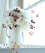 Close-up of white hydrangea and rose hips bouquet in white jug
