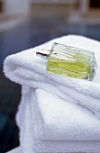 Green perfume bottle lying horizontal without lid on stack of white towels