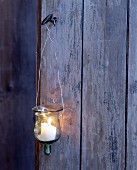 A glass lantern with a burning candle hanging on a wooden wall