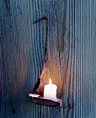 Alte Öllampe mit Stumpenkerze hängt an einem Haken an der Wand