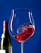 Geschwenktes Rotweinglas mit Rotwein vor blauem Hintergrund