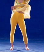 Woman in yellow outfit shaking hips while doing samba against blue background, low section