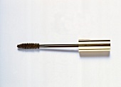 Close-up of mascara brush with golden cover placed on white background