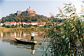Man standing in boat on river in front of castle and houses