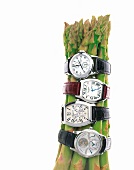 Close-up various luxury wrist watches on green asparagus against white background