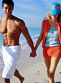 Happy couple walking hand in hand on  beach, smiling
