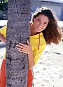 Bruenette Frau, Strand versteckt sich lachend hinterm Baum