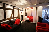 View of room with red sofa and bed, black sofa and white curtains at hotel in Germany