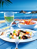 Fresh seafood salad on a plate, shrimp in bowl and glass of white wine on table