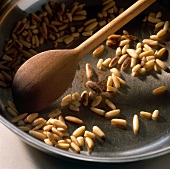 Pine nuts are roasted golden brown in a frying pan with wooden spoon