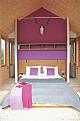Bedroom with gray bedsheet on bed, antlers on purple wall