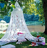 Floor cushions and decorative cushions under a romantic mosquito net by a lake