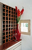 Großes Weinregal aus Kirschholz, davor eine rote Glasvase.
