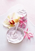 Close-up of white bowl with cream, cream container and three flowers on white background