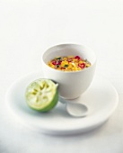 A white cup with mango salsa, along with a half lime on plate