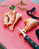 Four pieces of chicken with knife and herbs on chopping board