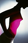 Silhouette of nude woman with pink light on abdomen