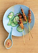 Sate skewers on plate with peanut sauce in spoon