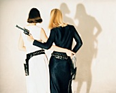 Rear view of two woman in black and white dress wearing revolver belts, holding revolver