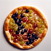 Pizza topped with green, blue and red grapes on white background