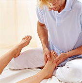Close-up of masseur pressing the thumb while holding ankle of woman for foot massage