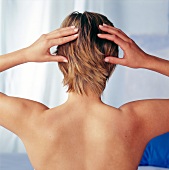 Rear view of blonde woman with short hair, massaging her head with fingertips