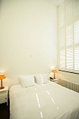 Bedroom with bed, cushion, side lamp and blinds in hotel, Netherlands