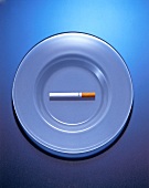 Eine Zigarette liegt auf einem Teller, blauer Hintergrund