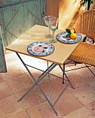 Plate, fruits and glass on folding table with wicker chair in garden terrace