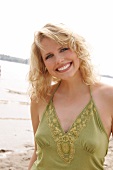 Portrait of beautiful blonde woman wearing green halter top standing on beach, smiling