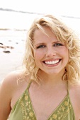 Portrait of beautiful blonde woman wearing green halter top standing on beach, smiling