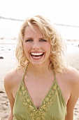 Portrait of beautiful blonde woman wearing green halter top standing on beach, smiling