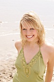 Portrait of beautiful blonde woman wearing green halter top standing on beach, smiling