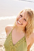 Portrait of beautiful blonde woman wearing green halter top standing on beach, smiling