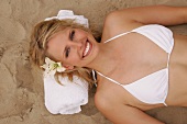 Overhead view of pretty woman in white bikini with flower in hair lying on sand, smiling