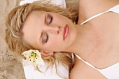 Close-up of peaceful woman with flower in hair lying on sand, eyes closed, overhead view