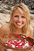 Berit Blonde Frau,.Schale voller bunter Blütenblätter am Strand