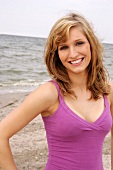 Portrait of beautiful woman wearing purple top standing on beach, smiling